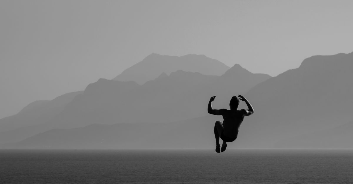 A silhouette of a diver in mid-air over the sea with mountains in Antalya, Türkiye.